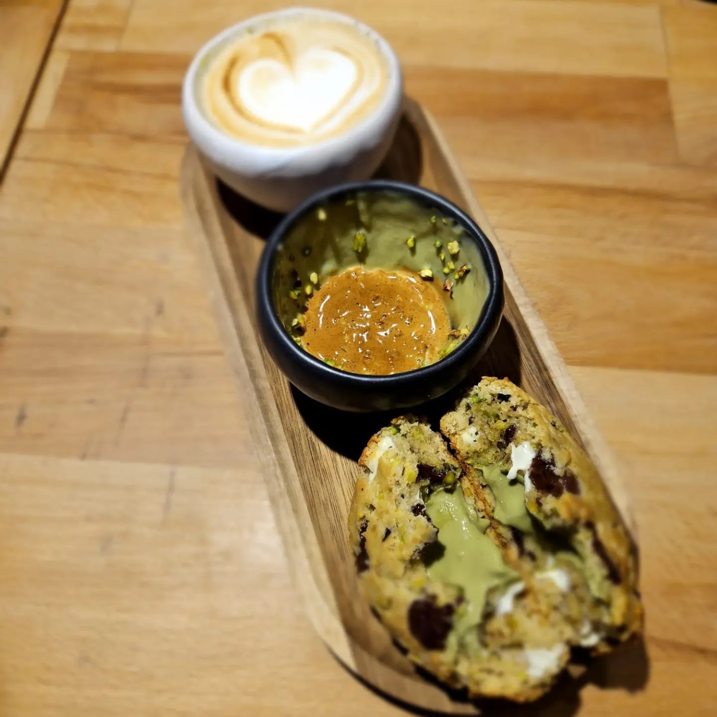 Cookie rupt în două, cu cremă de fistic, lângă un latte