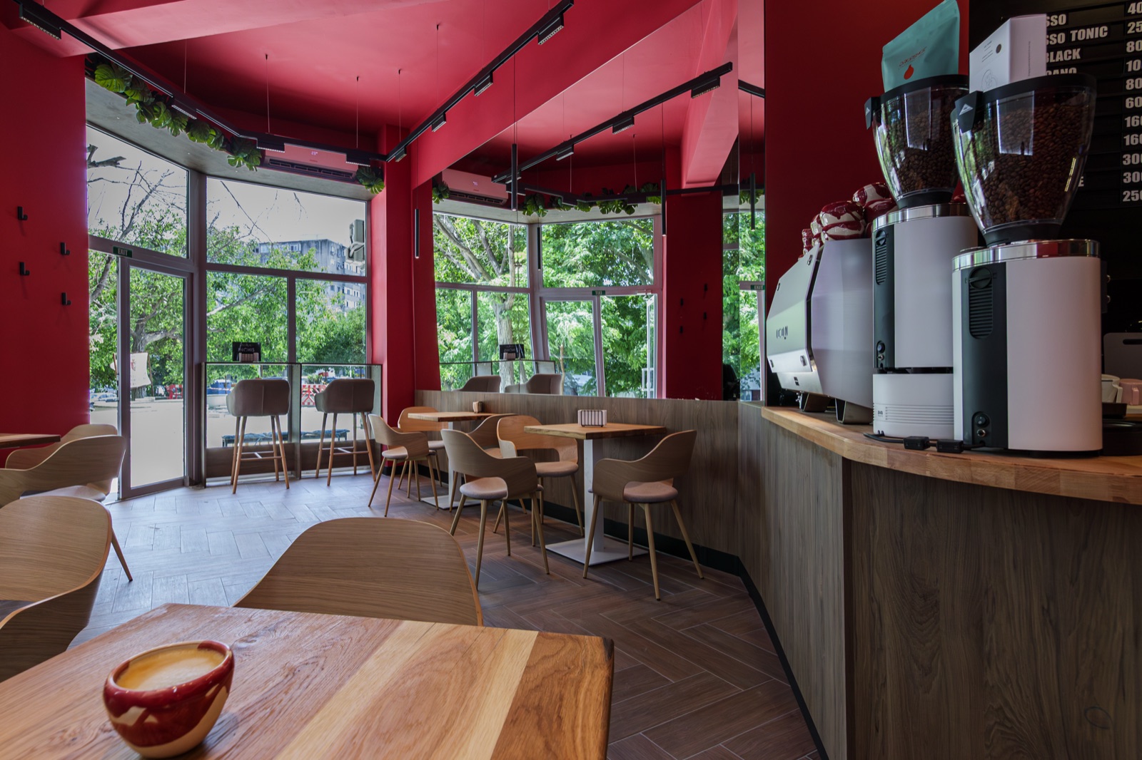Interiorul roșu al Nuruk Coffee Shop Boema, cu mese de lemn și ferestre mari spre bulevard